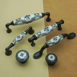 May include: A collection of cabinet handles and knobs. The black metal hardware features ceramic inserts with a repeating pattern of blue, white, and yellow geometric shapes. The set includes different handle sizes and knob styles for various cabinet types.