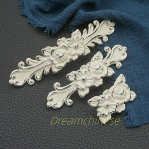 Op de afbeelding: Ivoor kleurige bloemenkastknoppen met zilveren accenten. De decoratieve hardware heeft een bloemenontwerp en sierlijke details. De afbeelding bevat drie stukken van verschillende grootte, met de tekst "Dreamchinese" onderaan.