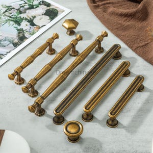 May include: A collection of antique brass cabinet hardware, including various sizes of handles and knobs. The hardware features a detailed, aged finish with a classic design, suitable for furniture restoration or new builds.