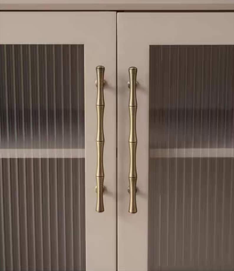 Op de afbeelding: Close-up van een kast met twee deuren. Elke deur heeft een helder glazen paneel met verticale lijnen en een bamboe-stijl messing handvat. De kastdeuren zijn lichtbeige.