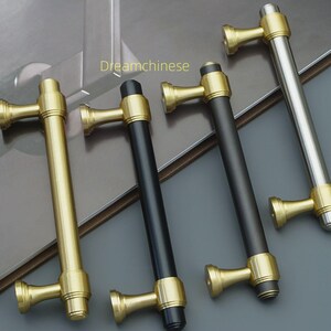 May include: Four cabinet pulls in gold, black, and silver. The pulls have a cylindrical bar with decorative end pieces. The text "Dreamchinese" is visible in the image.
