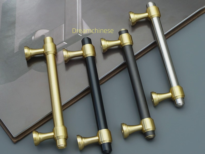 May include: Four cabinet pulls in gold, black, and silver. The pulls have a cylindrical bar with decorative end pieces. The text "Dreamchinese" is visible in the image.