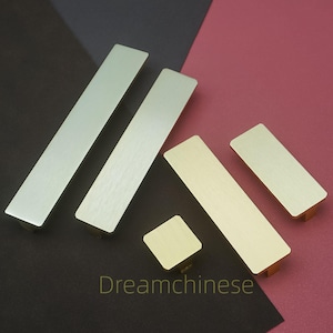 Op de afbeelding: Een verzameling rechthoekige en vierkante kastgrepen in diverse metallic afwerkingen. De grepen zijn in zilver- en goudtinten, met een geborstelde metaaltextuur. Het Dreamchinese-logo is zichtbaar onderaan.