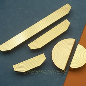 May include: A collection of gold-colored cabinet hardware, including long rectangular pulls, smaller angular pulls, and a circular knob. The hardware features a grooved design and is arranged on a blue and orange background. The text "dreamchinese" is visible.