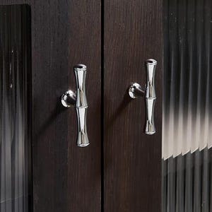 Op de afbeelding: Close-up van een donkerbruine houten kast met twee zilveren handgrepen in bamboevorm. De kastdeuren hebben een verticaal nerfpatroon en de handgrepen zijn aan de voorkant van de deuren bevestigd.