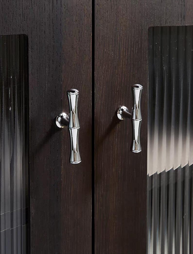 Op de afbeelding: Close-up van een donkerbruine houten kast met twee zilveren handgrepen in bamboevorm. De kastdeuren hebben een verticaal nerfpatroon en de handgrepen zijn aan de voorkant van de deuren bevestigd.