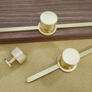 Pu&ograve; includere: Tre pezzi di ferramenta per mobili in ottone. Due pezzi hanno un pomello circolare con bordo scanalato e una lunga maniglia piatta. Il terzo &egrave; un piccolo pomello con bordo scanalato e gambo corto.