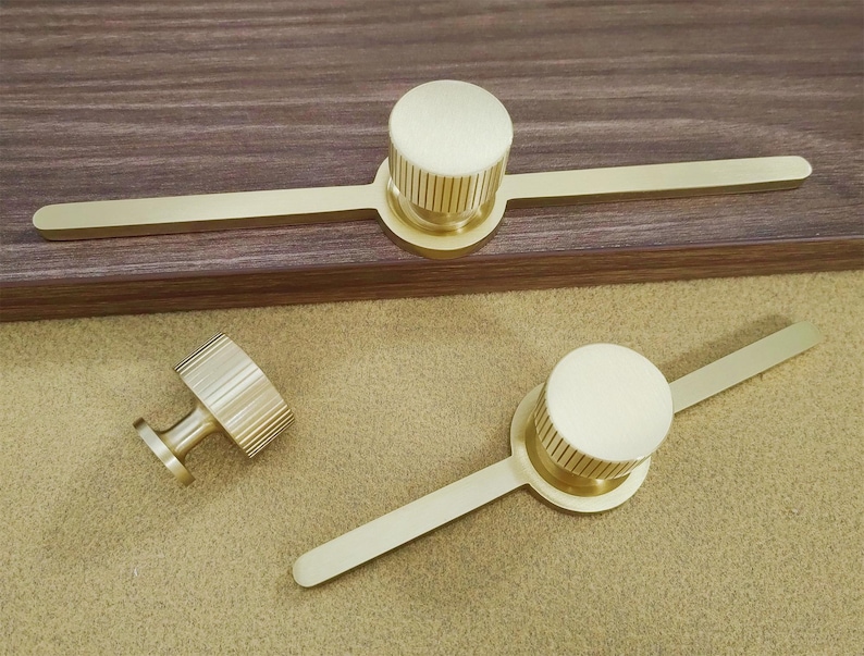 Pu&ograve; includere: Tre pezzi di ferramenta per mobili in ottone. Due pezzi hanno un pomello circolare con bordo scanalato e una lunga maniglia piatta. Il terzo &egrave; un piccolo pomello con bordo scanalato e gambo corto.