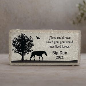 May include: A rectangular light gray stone memorial marker featuring a black silhouette of a horse standing under a tree with a bird flying above. The text reads: If love could have saved you, you would have lived forever, Big Dan, 2021.