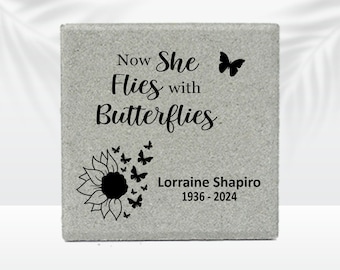 May include: A gray stone memorial with the words "Now She Flies with Butterflies" and a sunflower and butterfly design. The name "Lorraine Shapiro" and the years "1936-2024" are also inscribed on the stone.