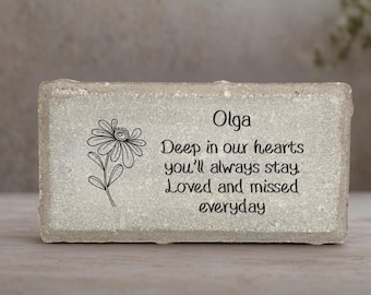 May include: A rectangular, light gray stone memorial with the name "Olga" and a floral illustration. The inscription reads "Deep in our hearts you'll always stay. Loved and missed everyday."