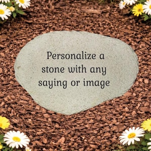 May include: A light gray, irregularly shaped stone with the text "Personalize a stone with any saying or image." The stone is surrounded by brown mulch and white and yellow daisies.