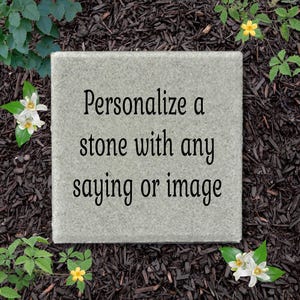 May include: A square, light gray stone paver featuring the black text "Personalize a stone with any saying or image" centered on its surface. The stone has a textured, natural finish and is positioned flat with clean, straight edges.