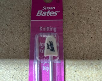 Può includere: Un paio di ferri da maglia Susan Bates nella confezione originale viola. I ferri presentano tappi terminali in plastica bianca con il logo Susan Bates stampato in nero. La confezione riporta il nome del marchio e il testo Knitting Needles in bianco.