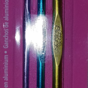 Puede incluir: Un juego de tres agujas de crochet de aluminio Susan Bates en morado, azul y dorado. Las agujas est&aacute;n etiquetadas con los tama&ntilde;os 4,0 mm (G-6), 5,0 mm (H-8) y 6,0 mm (J-10).
