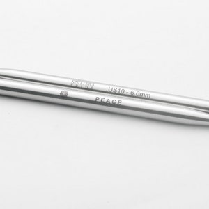 May include: A pair of silver knitting needles with the text "Knittery  Peace" and "US 10 - 6.0mm" printed on them.