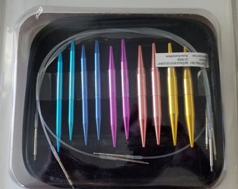 May include: A knitting needle set in a black zippered case, featuring thirteen pairs of interchangeable metal needles in blue, purple, pink, and yellow, along with four clear cables, stitch holders, connectors, and two tightening keys.