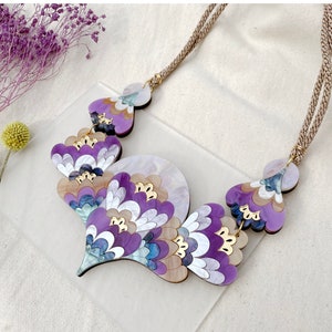 Könnte beinhalten: Eine violette, blaue und weiße Statement-Halskette mit einem mehrschichtigen, floralen Design. Die Halskette ist aus Holz gefertigt und hat ein natürliches, organisches Aussehen.