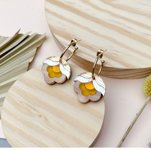 Könnte beinhalten: Ein Paar goldene Creolen mit einem weißen und gelben Blumendesign. Die Blumen haben einen geschichteten Look mit einer weißen Außenschicht und einer gelben Innenschicht.