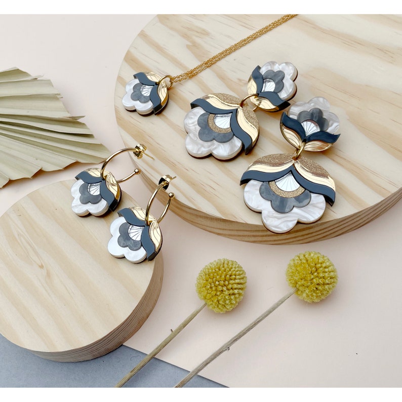 Pode incluir: Um conjunto de brincos florais pretos, brancos e dourados e um colar combinando. Os brincos s&atilde;o de argola com design floral e o colar tem um pingente com design floral.