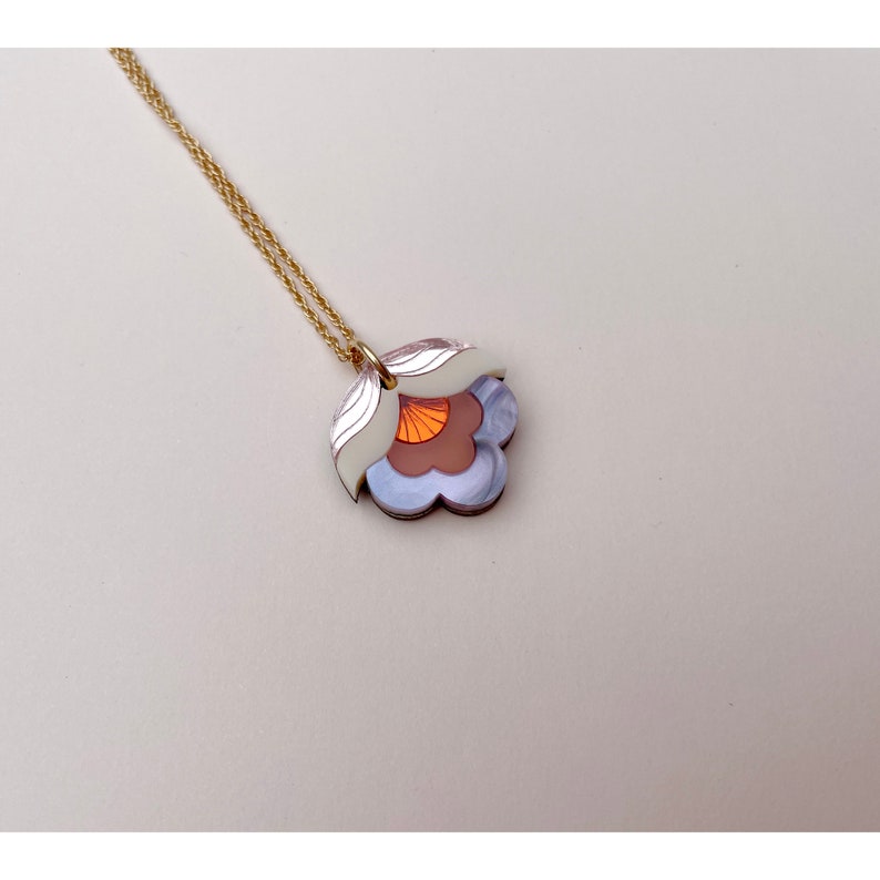 Pode incluir: Um colar de corrente dourada com um pingente de flor em camadas. A flor &eacute; feita de acr&iacute;lico branco, roxo e laranja.