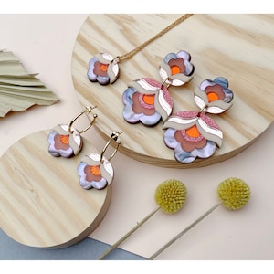Pode incluir: Um conjunto de brincos em forma de flor rosa, laranja e branca e um colar combinando. As joias s&atilde;o feitas de acr&iacute;lico e t&ecirc;m um design em camadas e dimensional.