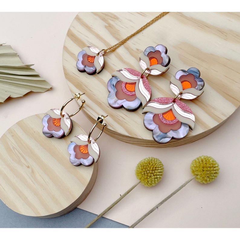 Pode incluir: Um conjunto de brincos em forma de flor rosa, laranja e branca e um colar combinando. As joias s&atilde;o feitas de acr&iacute;lico e t&ecirc;m um design em camadas e dimensional.