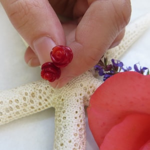 May include: A pair of red rose-shaped earrings. The earrings are made of a smooth, polished material and have a delicate, feminine design.