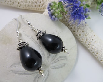 May include: A pair of black teardrop-shaped earrings with silver accents. The earrings are made of black onyx and silver.