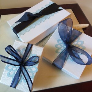 May include: Three white gift boxes with blue and white patterned paper. The boxes are tied with blue ribbon bows.