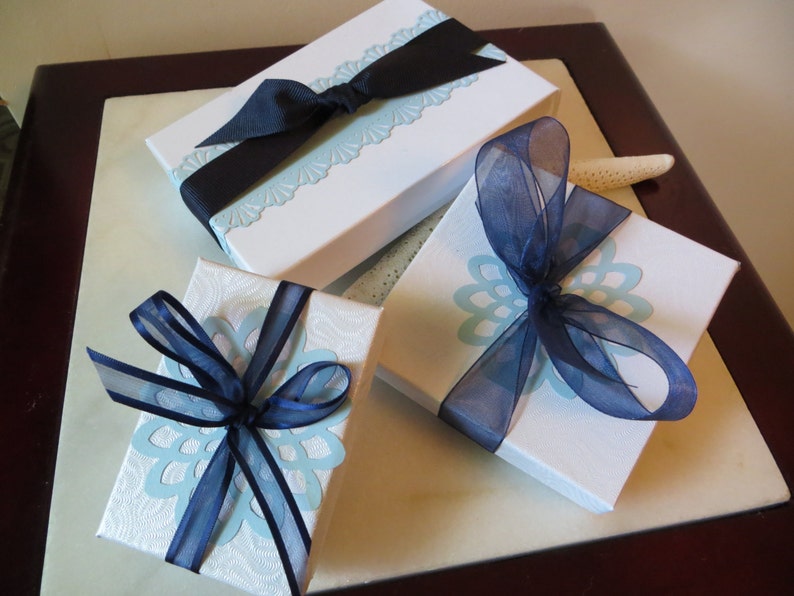 May include: Three white gift boxes with blue and white patterned paper. The boxes are tied with blue ribbon bows.
