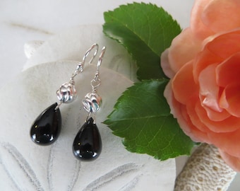 May include: A pair of silver dangle earrings with black teardrop-shaped stones and silver flower-shaped beads.