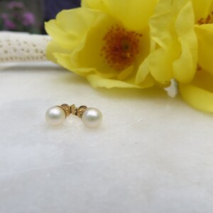 May include: A pair of pearl earrings with gold settings. The earrings are on a white surface.
