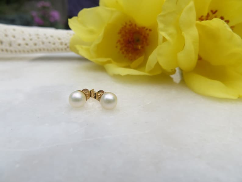May include: A pair of pearl earrings with gold settings. The earrings are on a white surface.