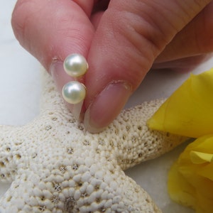 May include: A pair of pearl stud earrings with a white pearl and a gold setting. The earrings are shown on a white starfish.