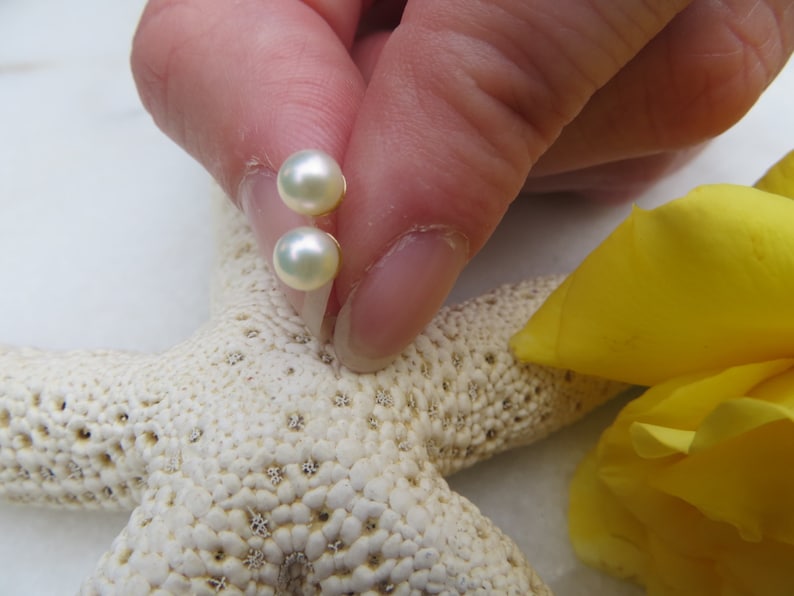 May include: A pair of pearl stud earrings with a white pearl and a gold setting. The earrings are shown on a white starfish.