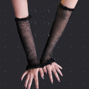 May include: Black, sheer arm warmers with a textured knit design and a fluffy trim at the top. The arm warmers are shown against a dark background with small white dots.