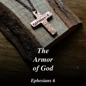 May include: A copper cross pendant with the inscription "Ephesians 6" hangs on a chain. The cross rests on a piece of wood. The text "The Armor of God" and "Ephesians 6" are displayed below the cross.
