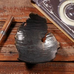 May include: A black metal tray shaped like the state of Michigan. The tray is sitting on a wooden surface.