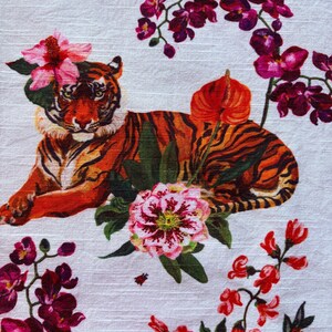 Puede incluir: Textil blanco con una ilustraci&oacute;n detallada de un tigre adornado con flores. El tigre tiene rayas naranjas y negras, con flores rosas y rojas y hojas verdes. Tambi&eacute;n se ve un colibr&iacute;.