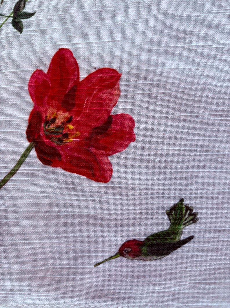 Puede incluir: Primer plano de una tela blanca con un tulip&aacute;n rojo y un colibr&iacute;. El tulip&aacute;n est&aacute; en plena floraci&oacute;n con un centro amarillo. El colibr&iacute; es rojo, verde y negro.