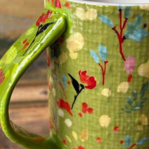 May include: Green ceramic mug with a floral pattern. The mug has a bright green handle and a white interior.