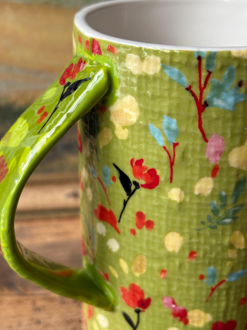 May include: Green ceramic mug with a floral pattern. The mug has a bright green handle and a white interior.