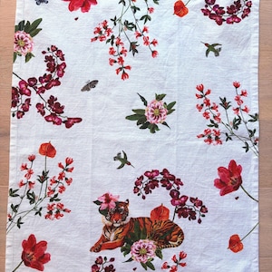 Puede incluir: Pa&ntilde;o de cocina rectangular blanco con un estampado floral y animal vibrante. El dise&ntilde;o presenta tulipanes rojos, orqu&iacute;deas, mariposas, colibr&iacute;es y un tigre. El tigre est&aacute; adornado con flores. El pa&ntilde;o est&aacute; hecho de un material suave y absorbente.