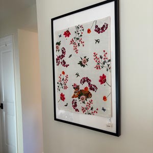 Puede incluir: Obra de arte enmarcada con un dise&ntilde;o floral. Flores rojas y rosas, mariposas y p&aacute;jaros sobre un fondo blanco. Incluye una ilustraci&oacute;n de tigre. El marco es negro.