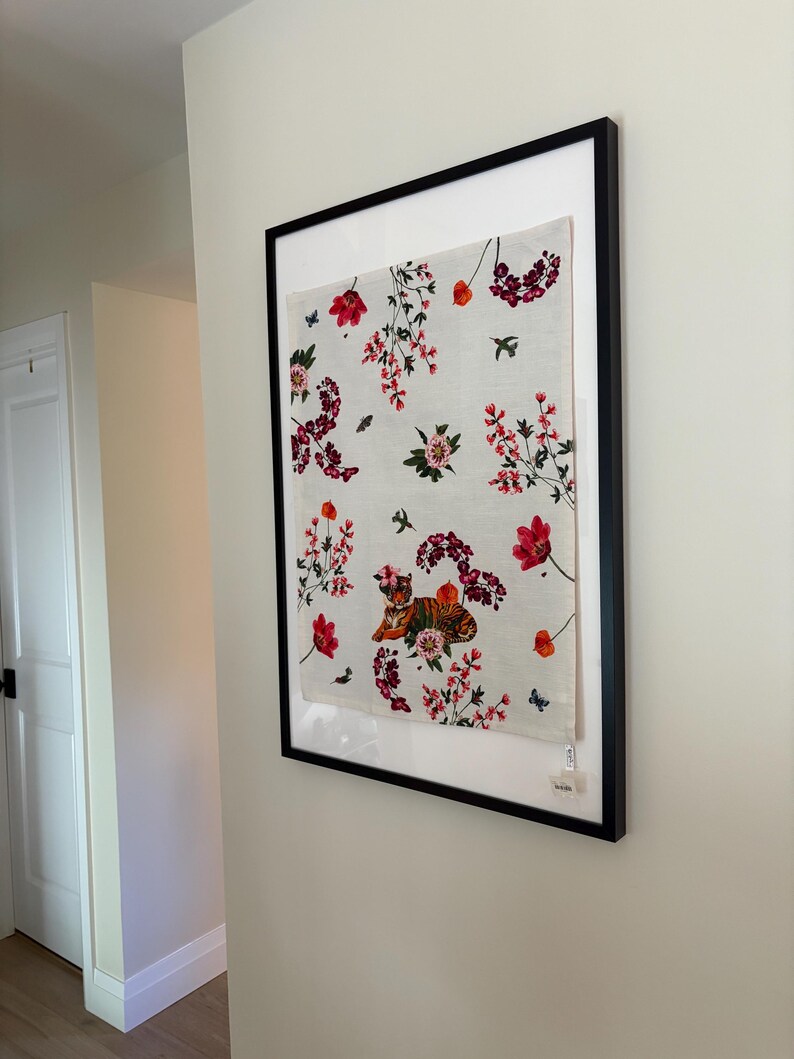 Puede incluir: Obra de arte enmarcada con un dise&ntilde;o floral. Flores rojas y rosas, mariposas y p&aacute;jaros sobre un fondo blanco. Incluye una ilustraci&oacute;n de tigre. El marco es negro.