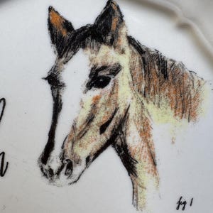 May include: White ceramic plate with a sketched horse head design. The horse is depicted in shades of brown, black, and white, with a detailed drawing of the horse's face. The plate has a scalloped edge.