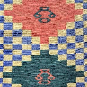 May include: Close-up of a woven textile with a repeating pattern. The design features a checkerboard of blue and beige squares, with two large, central shapes in red and teal. Each central shape has a smaller, decorative element.
