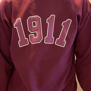 May include: A maroon sweatshirt with the number "1911" printed in white on the front.