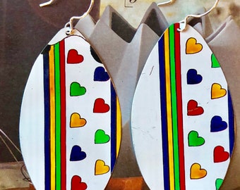 May include: A pair of oval-shaped earrings with a white background and colorful stripes and hearts. The earrings are made of metal and have silver hooks.
